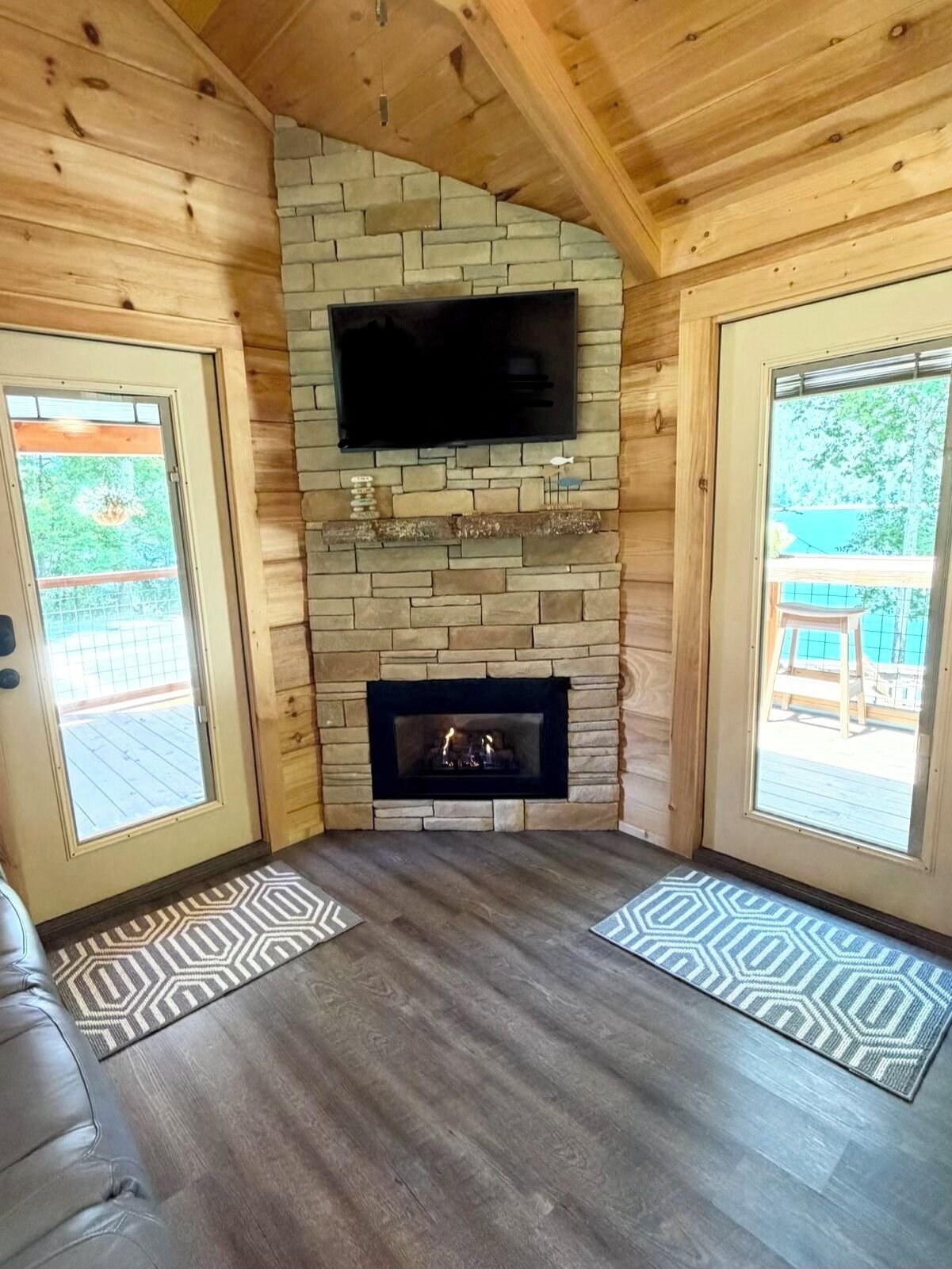 A room with a stone fireplace, a flat-screen TV mounted on the wall, and a wooden ceiling.