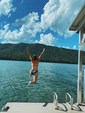 A woman jumping into a lake from a dock with a forested mountain in the background. - Bear Cub Cabin - Lakefront - Private Dock - Tritoon Boat Available for Rent (Butler)