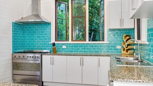 Une cuisine avec des meubles blancs, un fourneau et une fenêtre donnant sur des arbres.