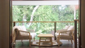 Un balcon agrémenté de meubles en osier et d’une table en bois, donnant sur un jardin luxuriant.