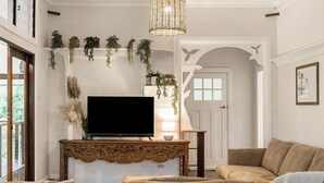 Un salon avec un téléviseur à écran plat posé sur une console en bois, un canapé beige et des plantes suspendues.