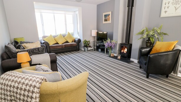A living room with a sofa, armchairs, a fireplace, and a striped carpet. - Seagull Cottage (Bude)