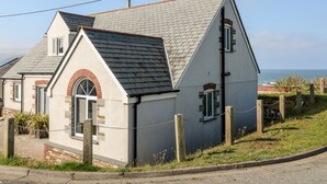 A coastal house with a sloped roof, a brick arch window, and a chain-link fence. - Seagull Cottage (Bude)