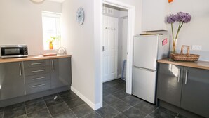 A modern kitchen with grey cabinets, a microwave, a refrigerator, and a clock on the wall. - Seagull Cottage (Bude)