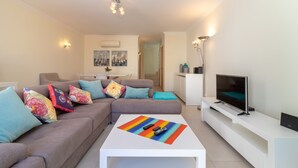 A modern living room with a sofa, a coffee table, a TV, and a white console table. - The Nest - Stunning sea views, communal pool & walking distance to beach (Carvoeiro)
