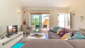 A living room with a TV, sofa, and coffee table. There is a sliding glass door leading to an outdoor area with a table and chairs. - The Nest - Stunning sea views, communal pool & walking distance to beach (Carvoeiro)