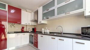 A modern kitchen with white cabinets, a red appliance, a stainless steel sink, and a microwave. - The Nest - Stunning sea views, communal pool & walking distance to beach (Carvoeiro)