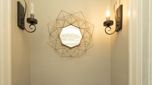 A hallway with a geometric wall decoration, two wall-mounted lights, and a round table with a glass top. - Cloverdale Large Group Duplex • 6BR • Sleeps 14 (Montgomery)