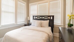 A bedroom with a bed, a nightstand, a dresser, and a window with blinds. - Cloverdale Large Group Duplex • 6BR • Sleeps 14 (Montgomery)