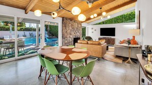 A modern living space with a dining area, a stone fireplace, a pool, and a TV mounted on the wall.