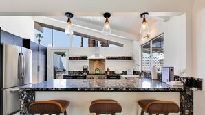 A modern kitchen with a large island, bar stools, stainless steel appliances, and pendant lighting.