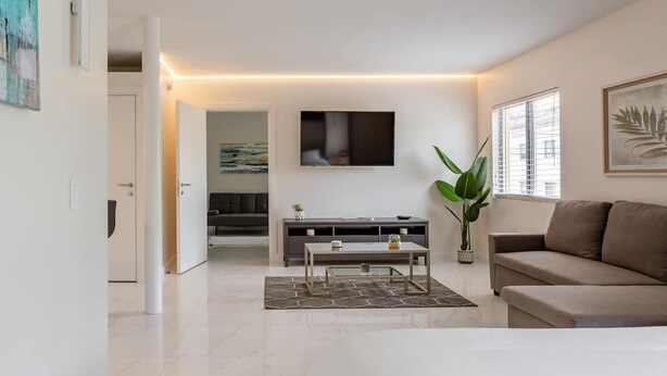Ein modernes Wohnzimmer mit Sofa, Couchtisch, Wandfernseher und einer Zimmerpflanze.