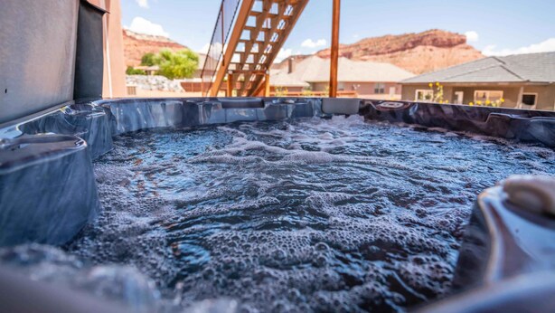 A hot tub with a wooden deck structure and a view of buildings and mountains in the background. - Sleeps 30! Kanab Retreat | Hot Tub & Theater (Kanab)