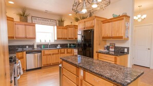 A modern kitchen with wooden cabinets, granite countertops, stainless steel appliances, and a central island. - Sleeps 30! Kanab Retreat | Hot Tub & Theater (Kanab)