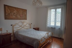 Une chambre à coucher avec un lit, une table de chevet, une lampe, un tableau et une fenêtre avec des rideaux.