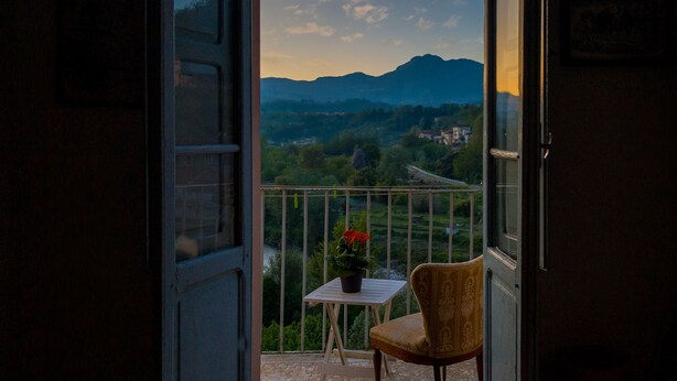 Eine geöffnete Tür, die auf einen Balkon mit Tisch, Stuhl und einer Topfpflanze führt.