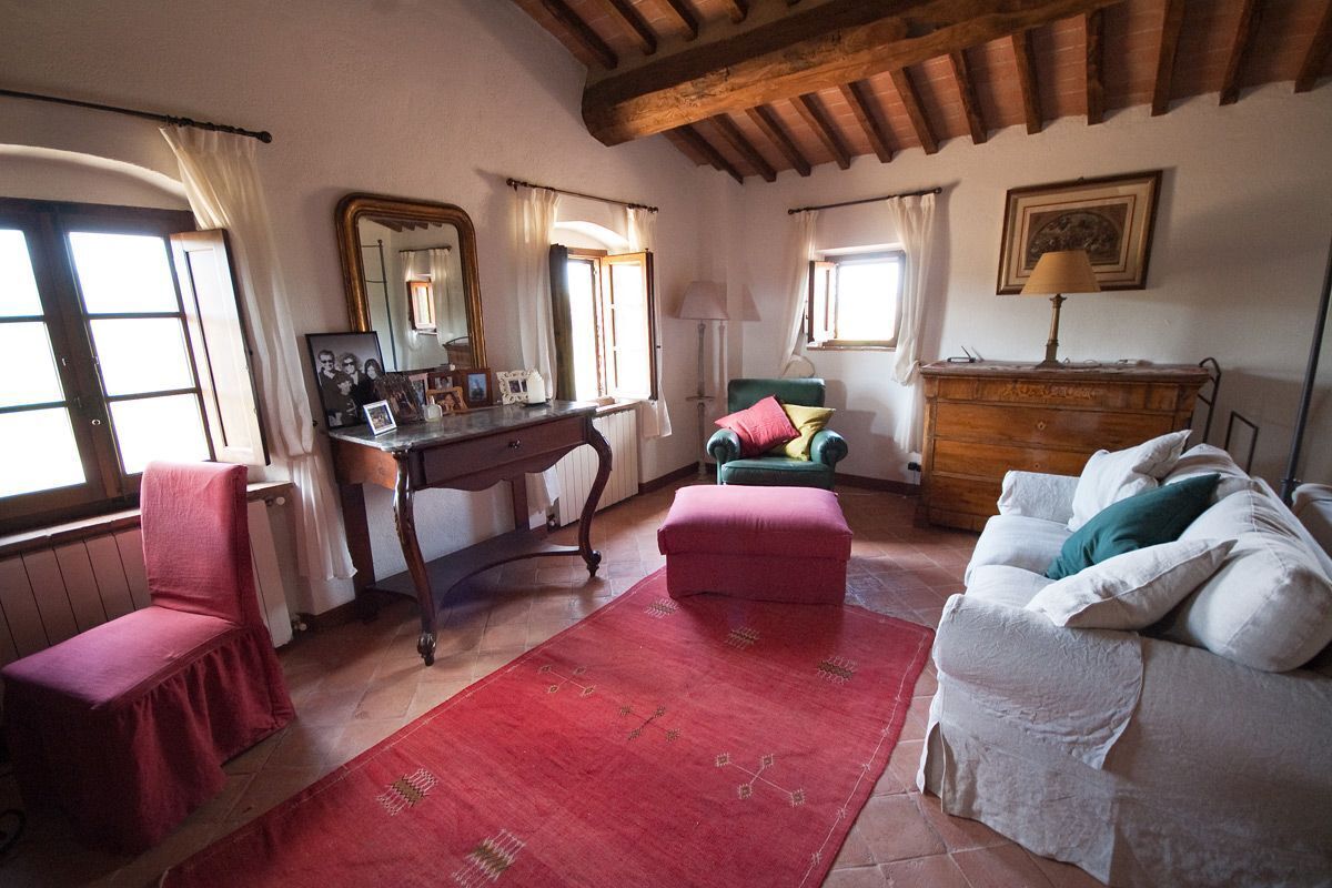 A cozy room with a wooden ceiling, a red rug, a white sofa, a green chair, and a wooden dresser.