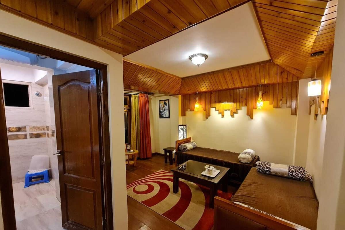 Una habitación acogedora con techo de madera, una mesa de comedor con sillas, un sofá y una mesita de noche con una lámpara.