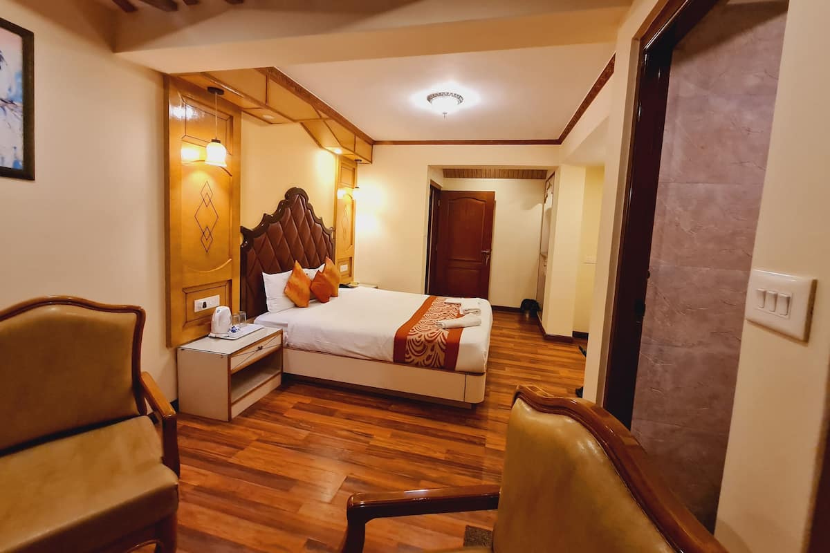 Una habitación de hotel con piso de madera, una cama con cabecera, una mesita de noche, una silla y una puerta.