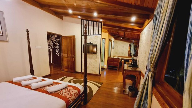 Quarto de hotel com uma cama, teto de madeira, área de jantar e cozinha visível por uma porta aberta.