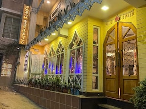 A building with a sign reading 'Omega Residency,' featuring a balcony with a railing, a series of windows with decorative glass, and a door with a metal gate. - Omega Residency (Darjeeling)