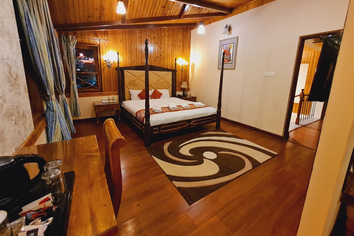 Una cama con dosel, un cabecero, mesitas de noche, un banco de madera, una alfombra y vistas de la ciudad de noche.