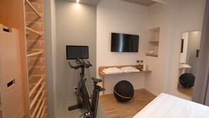 A modern hotel room with a wooden staircase, a stationary bike, a TV, a mirror, and a neatly made bed.