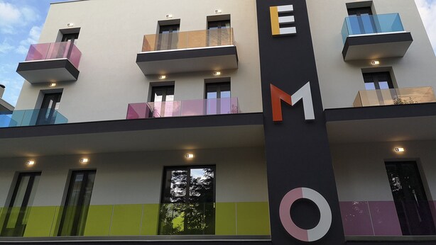 A modern building with balconies and a vertical sign with letters.