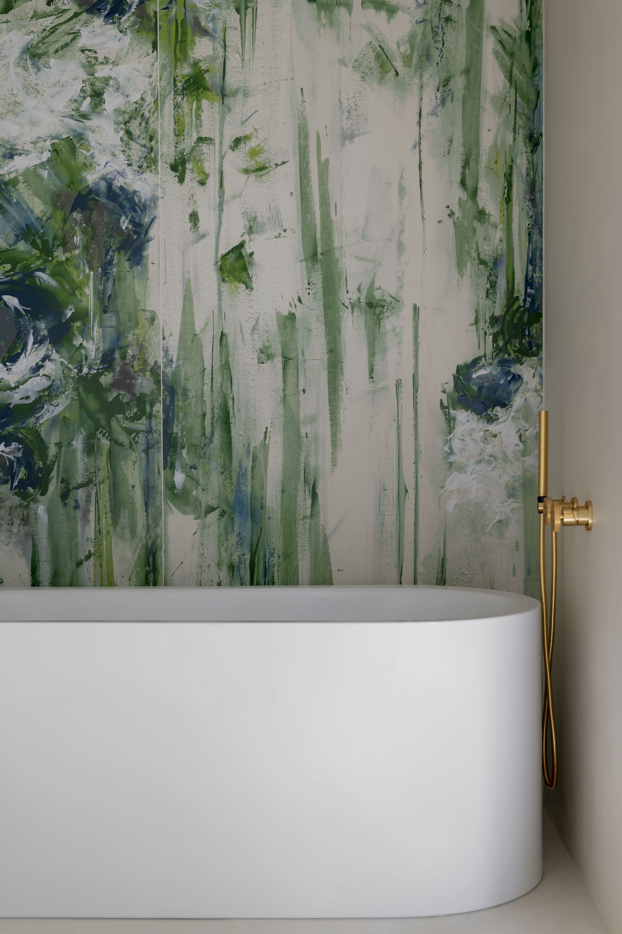 Ein modernes Badezimmer mit einer weißen Badewanne, einem goldenen Duschkopf und einer Wand mit abstrakter Grün-Weiß-Kunst.