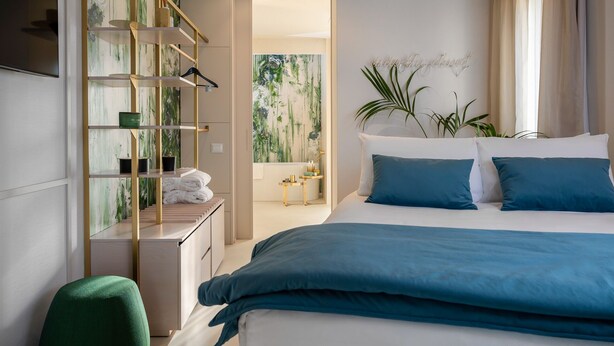 Et moderne hotelværelse med en stor seng, indbygget garderobeskab, et lille skrivebord og udsigt til grøn natur gennem vinduet.