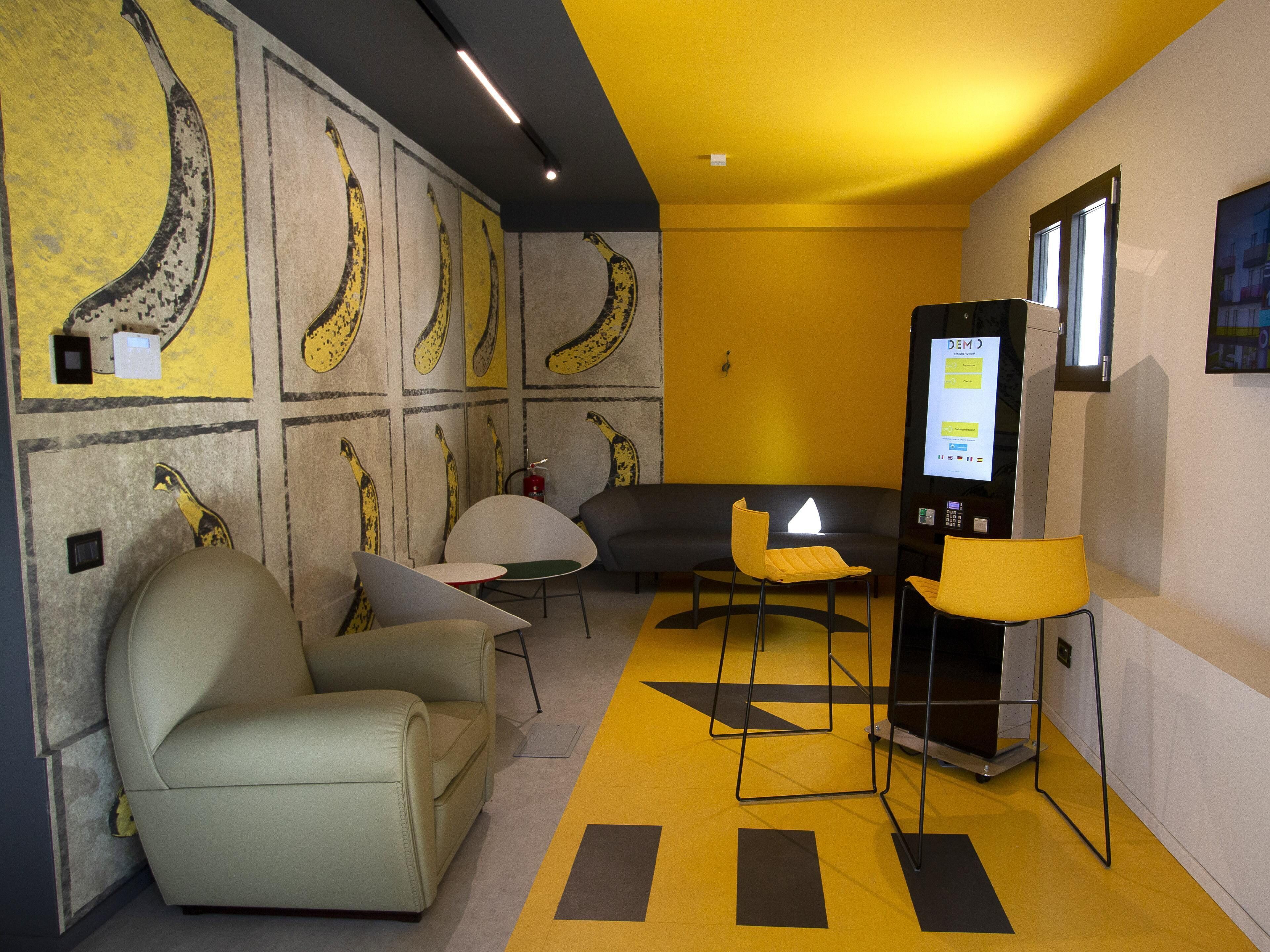Une pièce moderne aux couleurs jaune et gris, comprenant un canapé, des fauteuils, une petite table et un distributeur automatique.