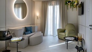 En moderne stue med sofa, rundt spejl, kaffemaskine, lille bord med en bog, en dekorativ plante og et fjernsyn.