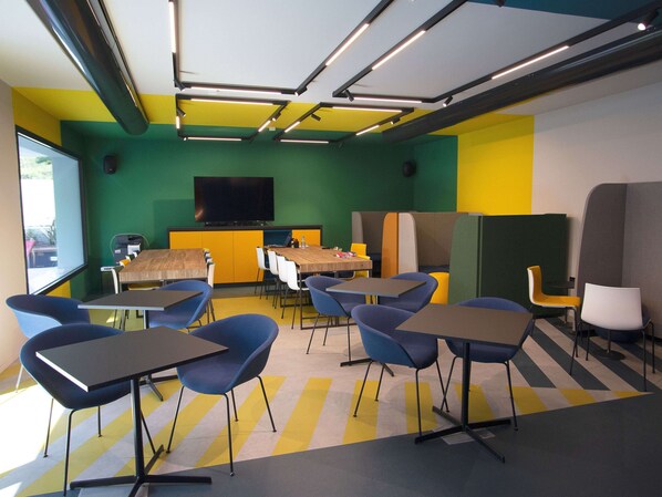 Une salle de conférence dotée d’une grande table, de nombreuses chaises, d’un téléviseur et d’un mur aux couleurs vives.