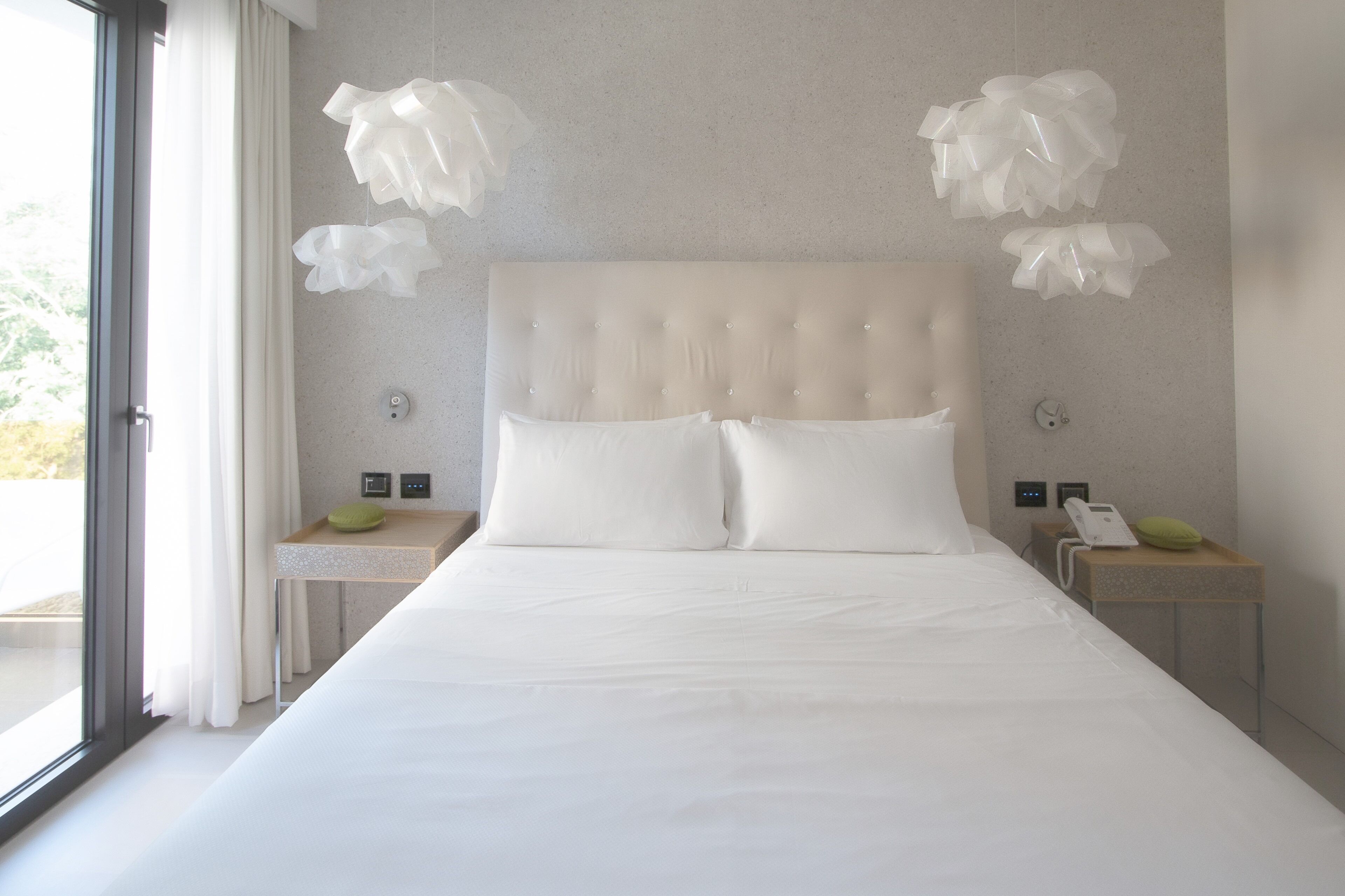 A modern hotel room with a large bed, two bedside tables, a telephone, and a window with curtains.