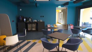 A modern lounge area with seating, a coffee station, and a view of the outdoors. - In A Light Wave: Il mare, l’acqua. Flexibility and inclusiveness (Rimini)