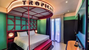 Una habitación de hotel con cama, escritorio, televisor y ventana con cortinas.