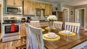 Una cocina moderna con armarios de madera, electrodomésticos de acero inoxidable y una mesa de comedor dispuesta con individuales y un jarrón de flores.