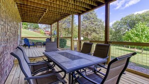 Un patio techado al aire libre con una mesa y sillas, techo de madera y vistas a un área verde con árboles.