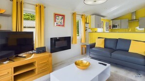 Uma sala de estar moderna com televisão de tela plana, sofá, mesa de centro e área de jantar com cortinas amarelas.