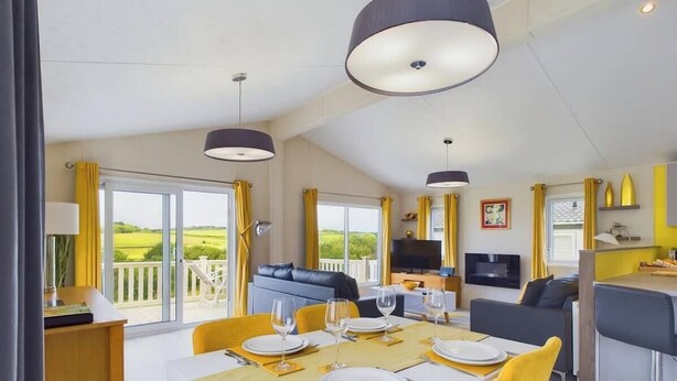 Uma sala de estar ampla com uma mesa de jantar posta para quatro pessoas, um sofá e uma televisão.
