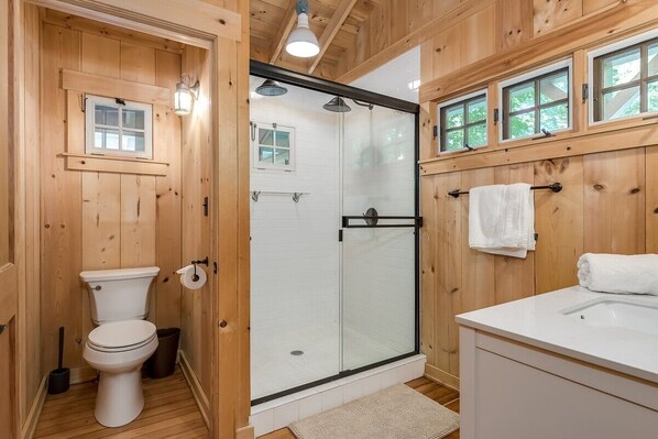 Ein Badezimmer mit Holzverkleidung, einer Toilette, einer Duschkabine und einem Waschbecken mit Handtuchhalter.