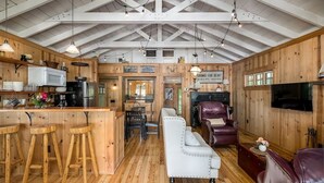 A rustic cabin interior with a kitchen, dining area, and seating space. - Dune-Top Harbor Views / Big Red Cottage + Hot Tub / Treetops (Saugatuck)