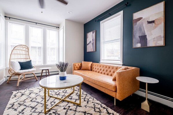A living room with a sofa, a round coffee table, a wicker chair, and a small side table. - ★ Modern Renovation ★ 10-Bedrooms! Perfect For Large Groups! (Providence)