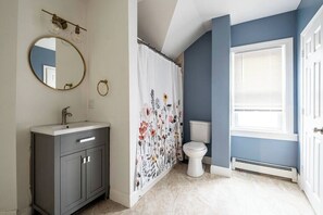 A bathroom with a gray vanity, a round mirror, a toilet, and a shower curtain with floral patterns. - ★ Modern Renovation ★ 10-Bedrooms! Perfect For Large Groups! (Providence)