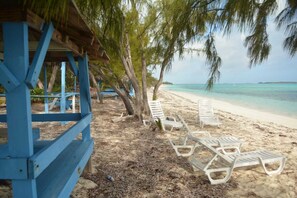 Une plage avec des chaises longues blanches et une structure bleue.