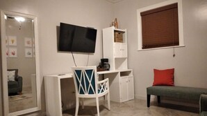 Habitació amb televisió penjada a la paret, escriptori amb cadira, una banca i un armari.
