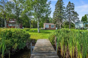 Un sentier en bois mène à une petite maison entourée d’une végétation luxuriante et d’arbres.