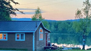 Puuinen mökki, jonka yhteydessä on laituri, ja joka sijaitsee järven rannalla puiden ja kukkuloiden ympäröimänä.