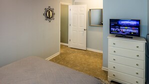 Un dormitorio con cama, cómoda, televisor y puerta que da a otra habitación.