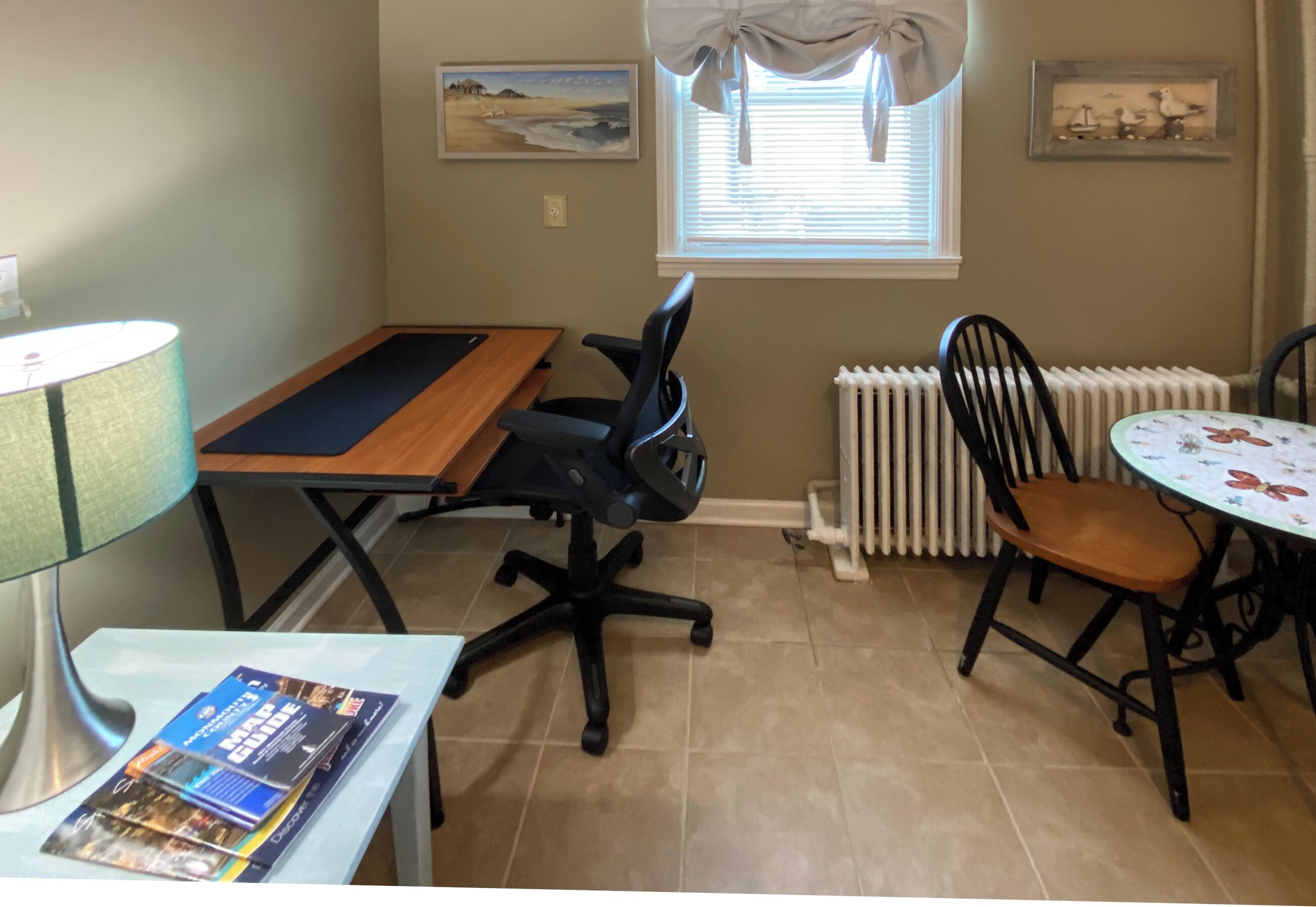 A room with a dining table, a computer desk, a chair, a lamp, and a radiator.